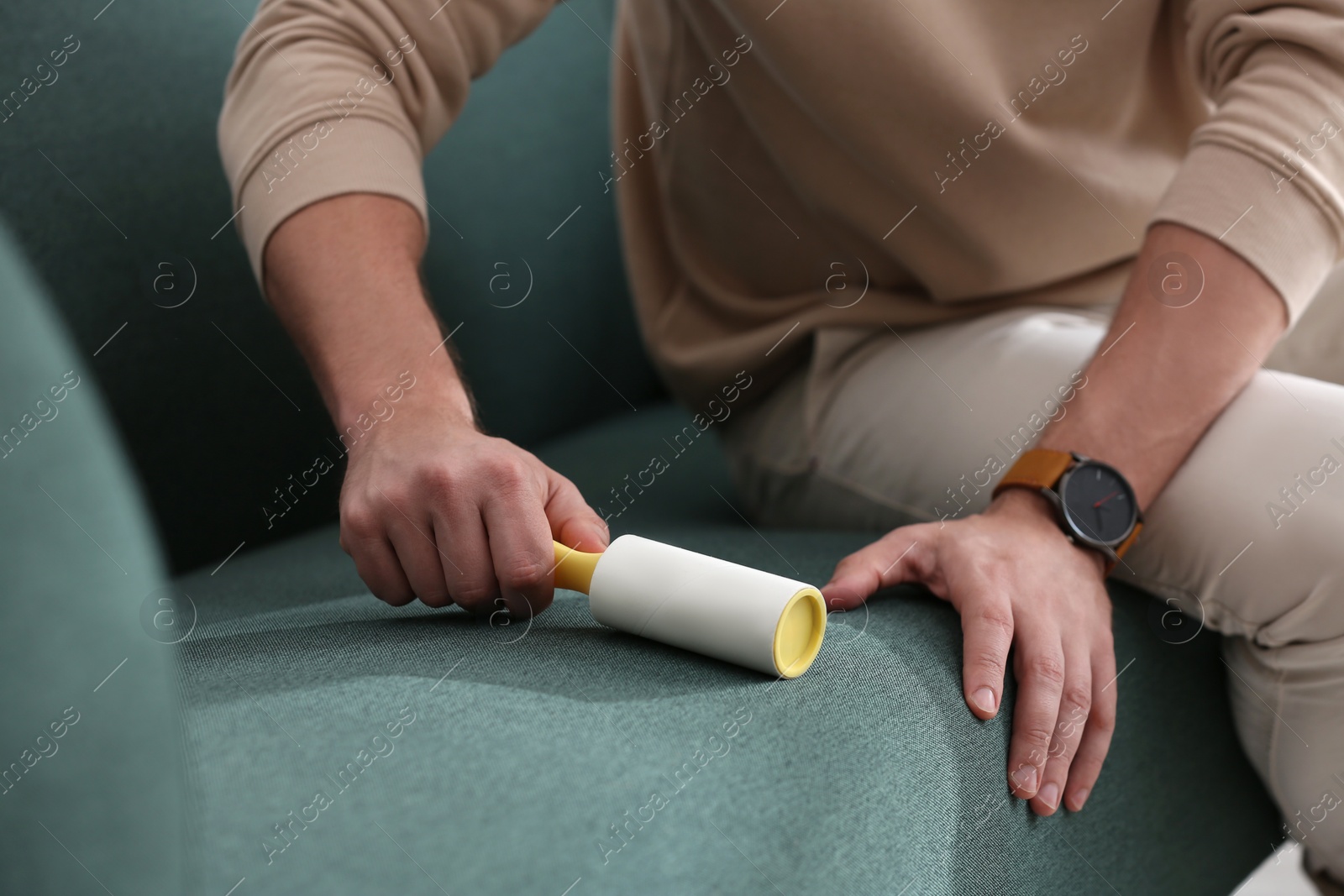 Photo of Man cleaning sofa with lint roller indoors, closeup