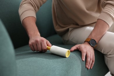 Photo of Man cleaning sofa with lint roller indoors, closeup