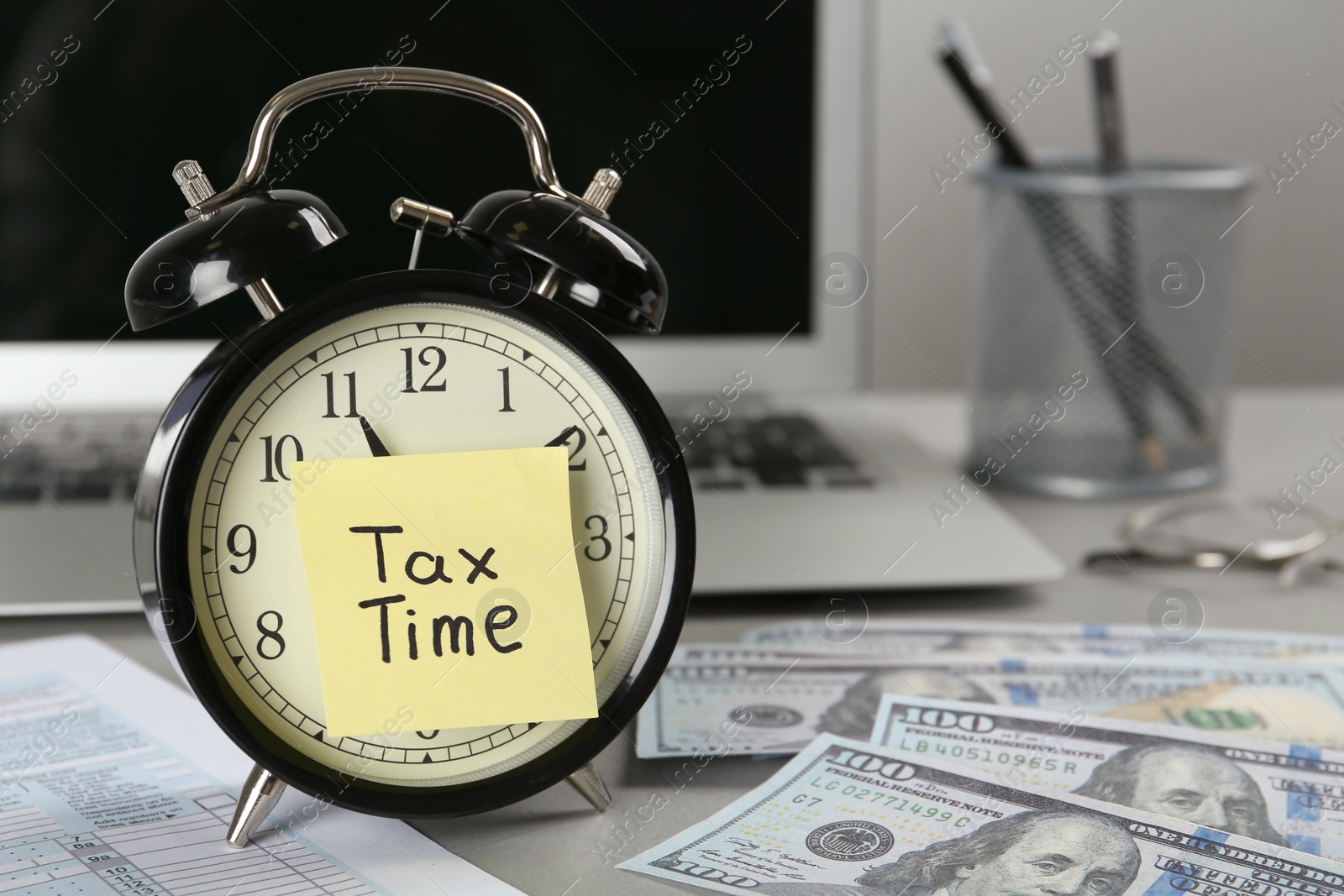 Photo of Alarm clock and reminder note with words Tax Time near laptop on grey table. Space for text