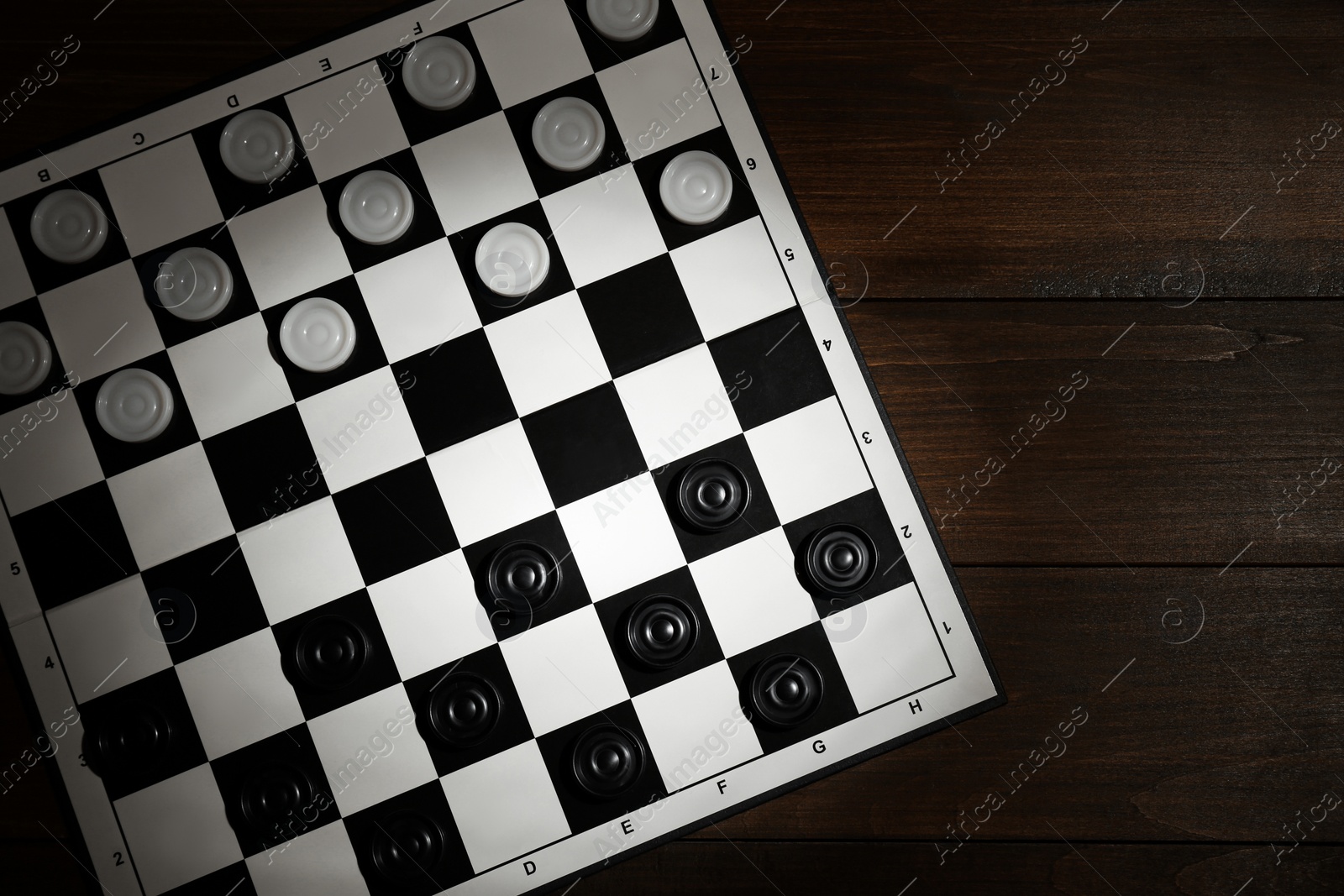 Photo of Checkerboard with game pieces on wooden table, top view