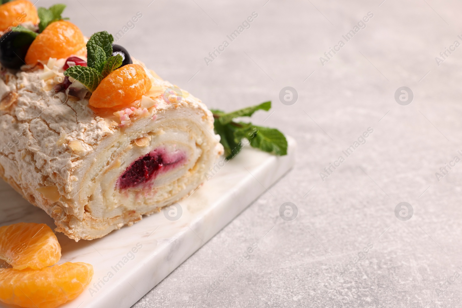 Photo of Tasty meringue roll with jam, tangerine slices and mint leaves on grey table, closeup. Space for text