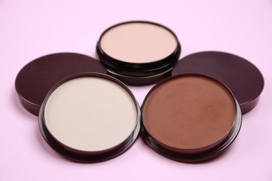 Photo of Different face powders on pink background, closeup