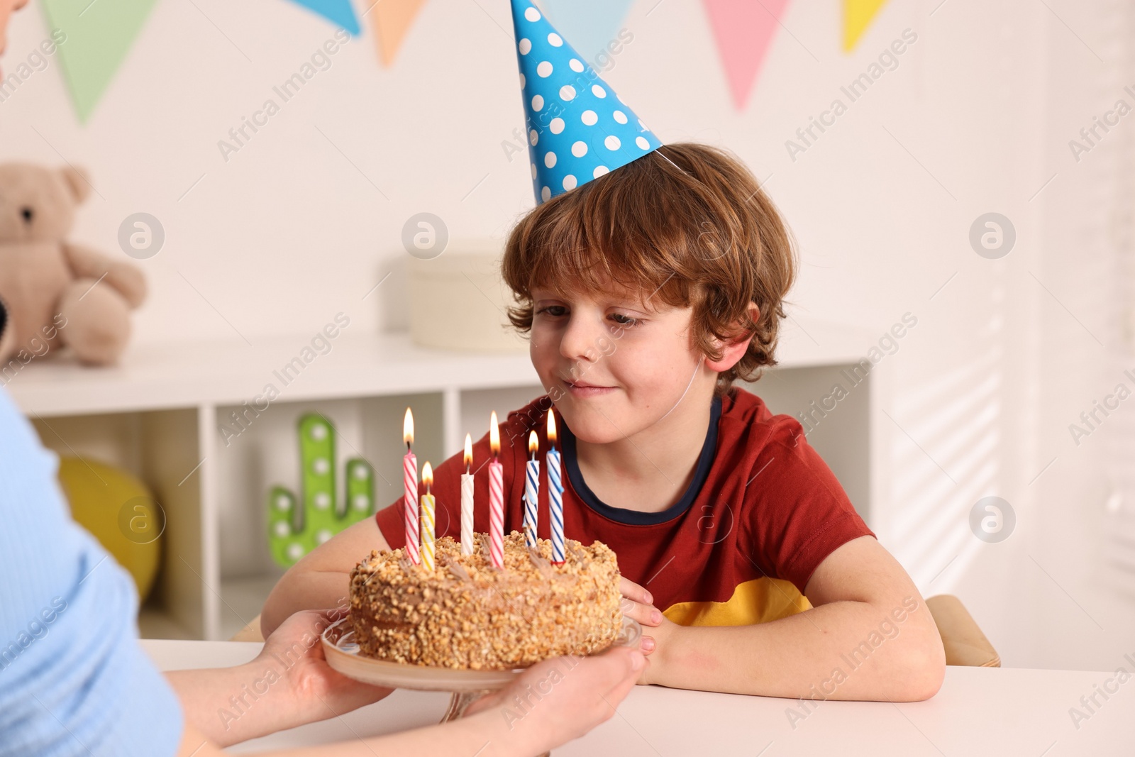 Photo of Birthday celebration. Mother holding tasty cake with burning candles near her son indoors