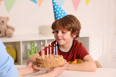 Birthday celebration. Mother holding tasty cake with burning candles near her son indoors