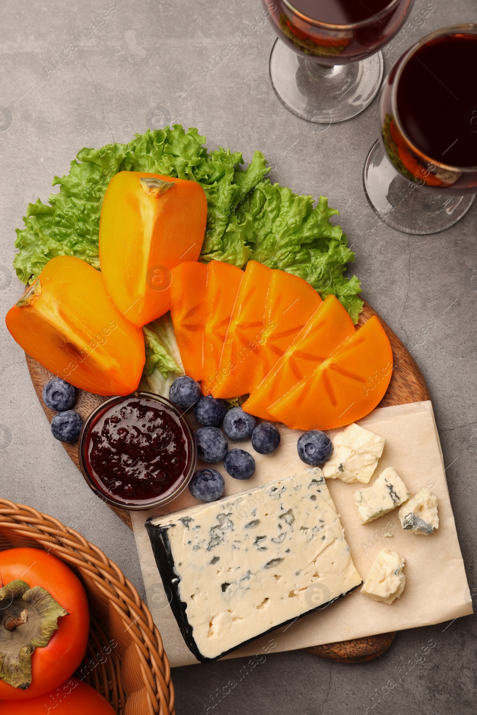 Photo of Delicious persimmon, blue cheese, blueberries and jam served on light grey table, flat lay