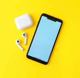 Photo of Wireless earphones, mobile phone and charging case on yellow background, flat lay. Space for text