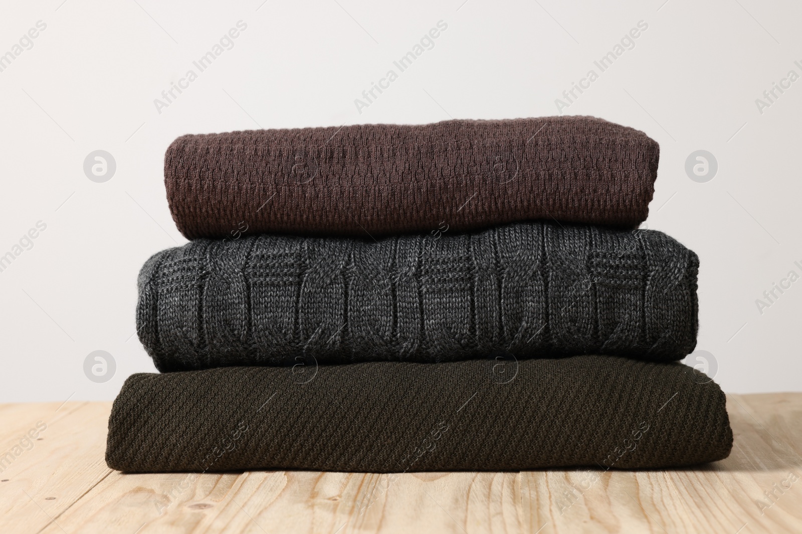 Photo of Stack of casual sweaters on wooden table against light background