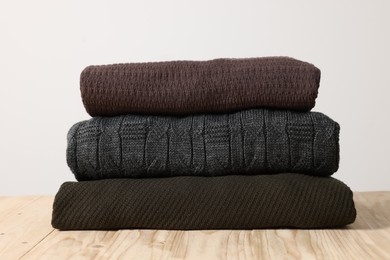 Photo of Stack of casual sweaters on wooden table against light background