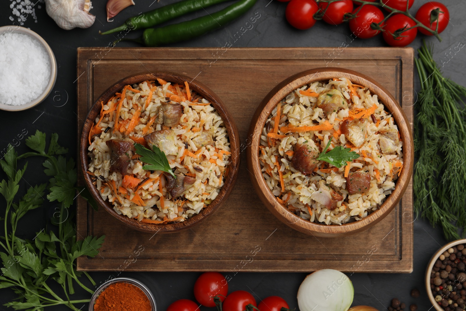 Photo of Delicious pilaf in bowls and products on black table, flat lay