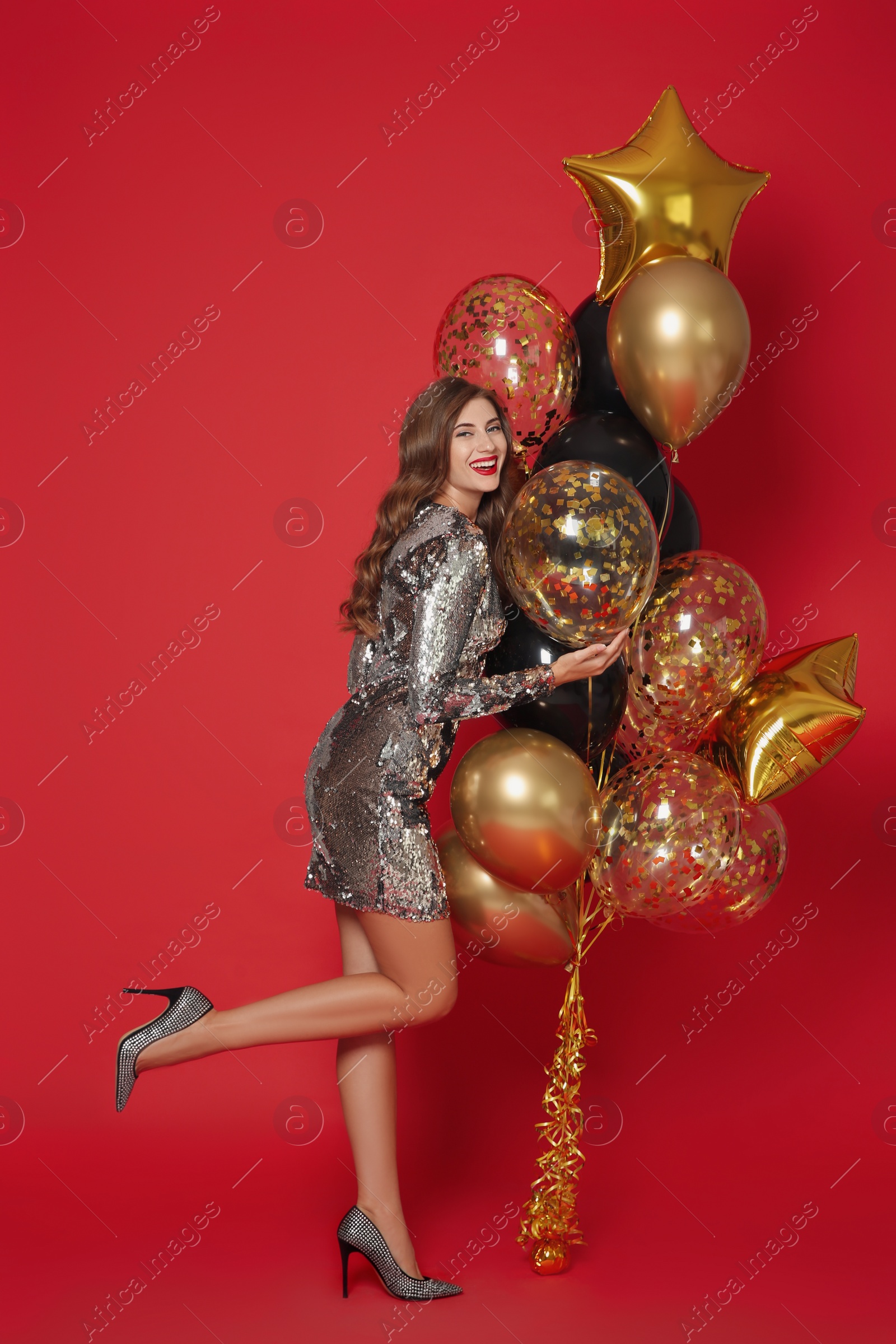 Photo of Happy woman in silver shiny dress with air balloons on red background. Christmas party