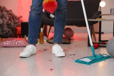 Photo of Man with mop cleaning messy room after New Year party, closeup of legs