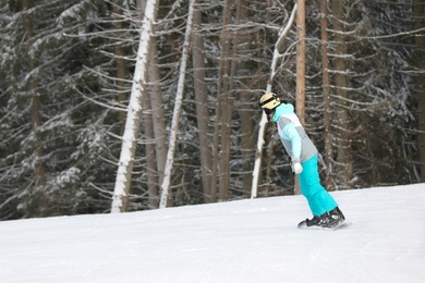 Woman in suit snowboarding on hill, space for text. Winter vacation