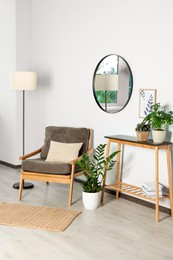 Stylish living room interior with wooden furniture, houseplants and round mirror on white wall