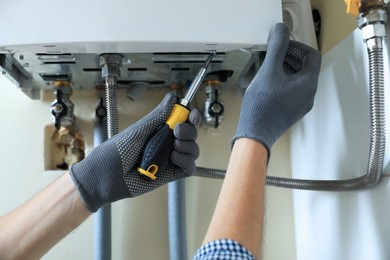 Photo of Man repairing gas boiler with screwdriver indoors, closeup