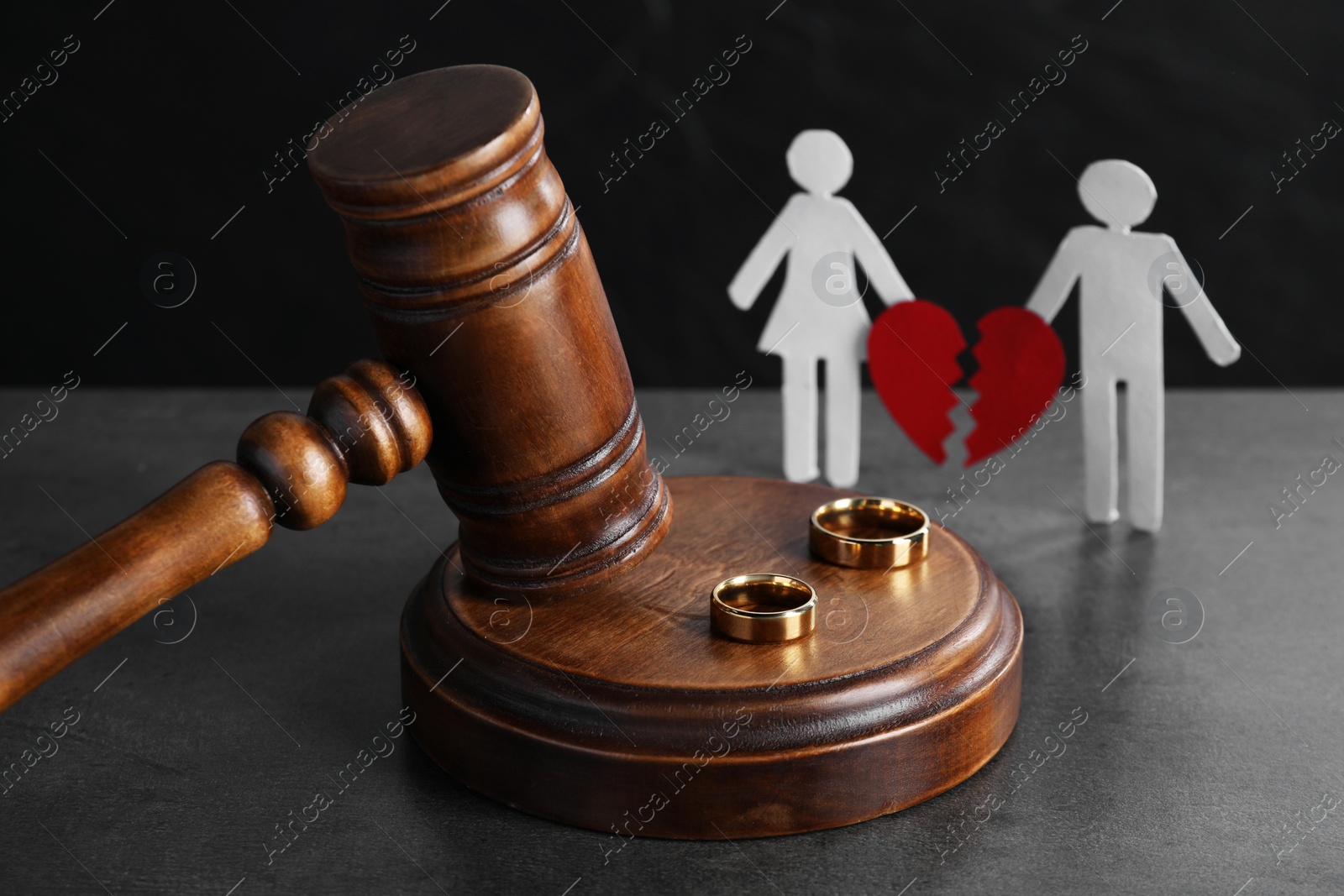 Photo of Divorce concept. Wooden gavel, wedding rings and paper cutout of couple with broken red heart on grey table