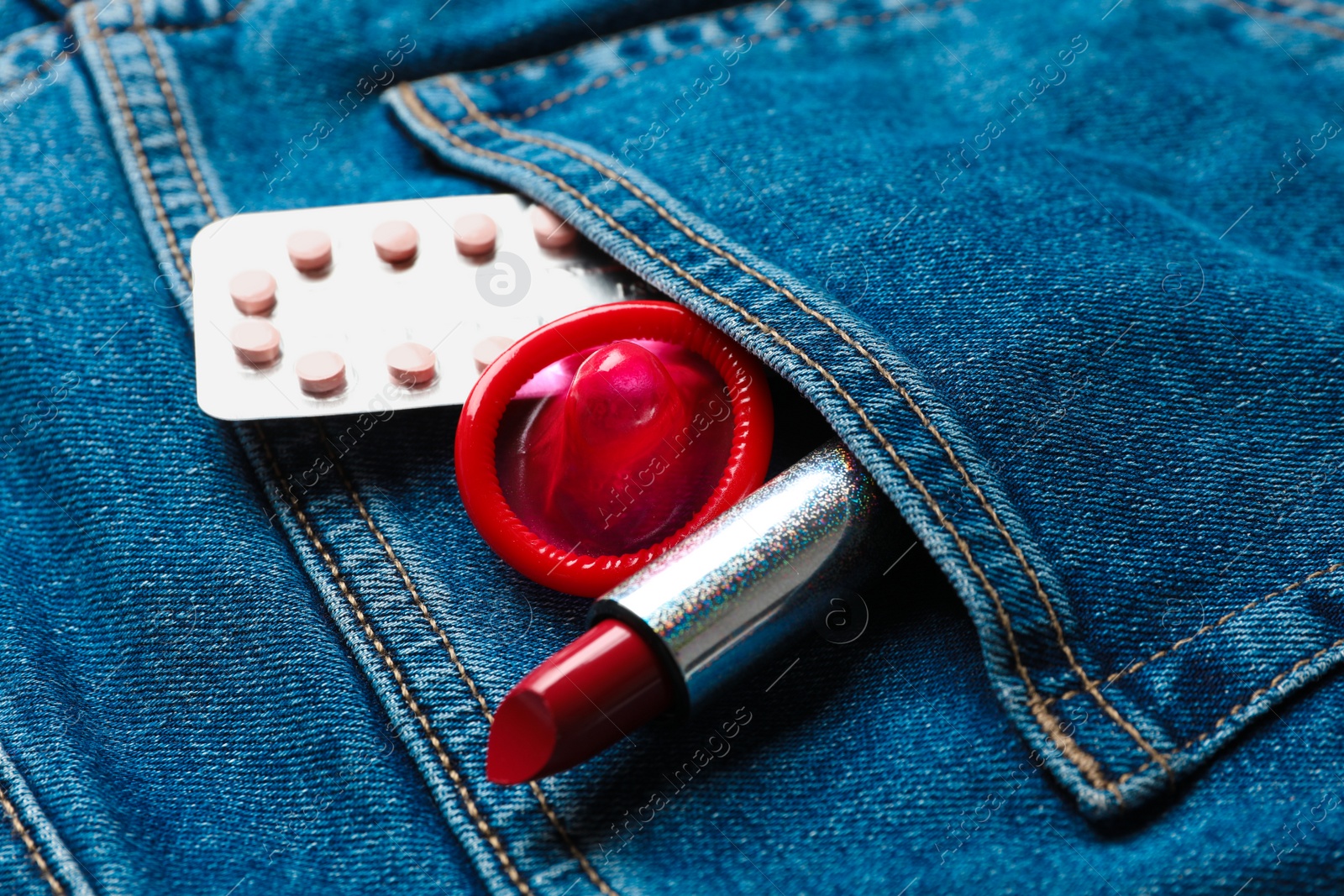 Photo of Red lipstick with condom and birth control pills in pocket of jeans, closeup. Safe sex concept