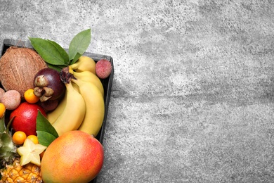 Photo of Different tropical fruits in wooden box on grey background, top view. Space for text