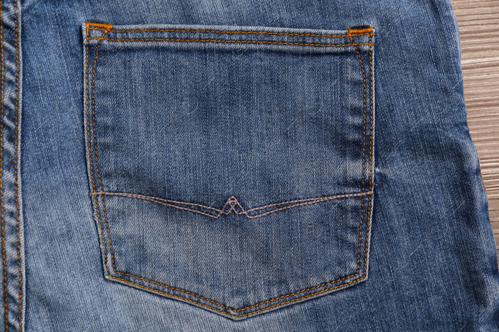 Photo of Stylish light blue jeans on wooden background, closeup of back pocket