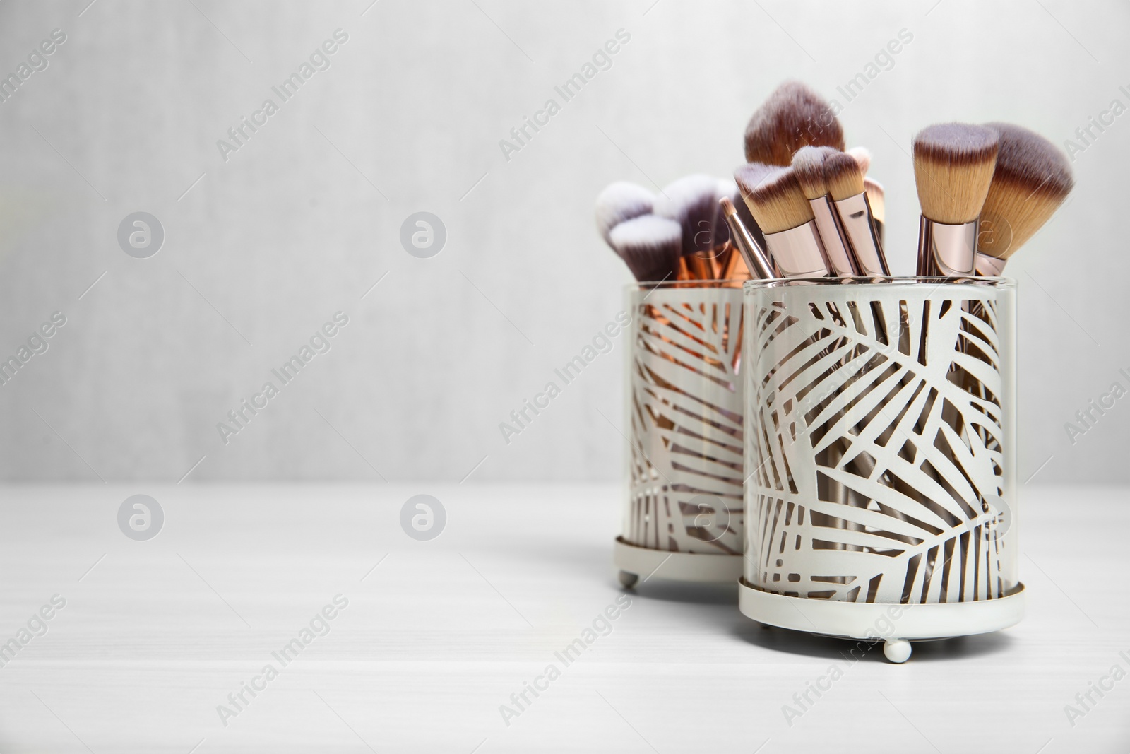 Photo of Organizers with professional makeup brushes on light table. Space for text