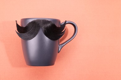 Photo of Man's face made of artificial mustache and cup on pink background, top view. Space for text