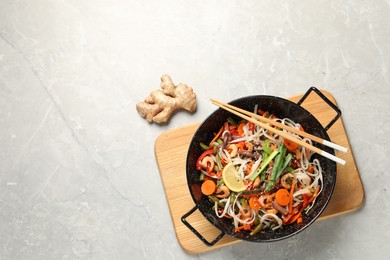 Photo of Shrimp stir fry with noodles and vegetables in wok on grey table, top view. Space for text