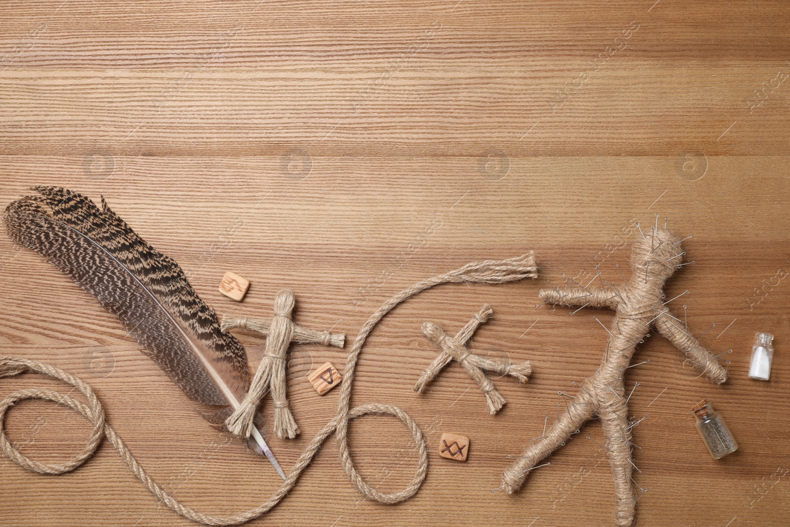 Photo of Voodoo doll pierced with pins and ceremonial items on wooden table, flat lay. Space for text