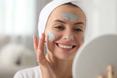 Photo of Young woman applying face mask in frontmirror indoors. Spa treatments