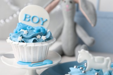 Photo of Delicious cupcake with light blue cream and Boy topper for baby shower on stand, closeup