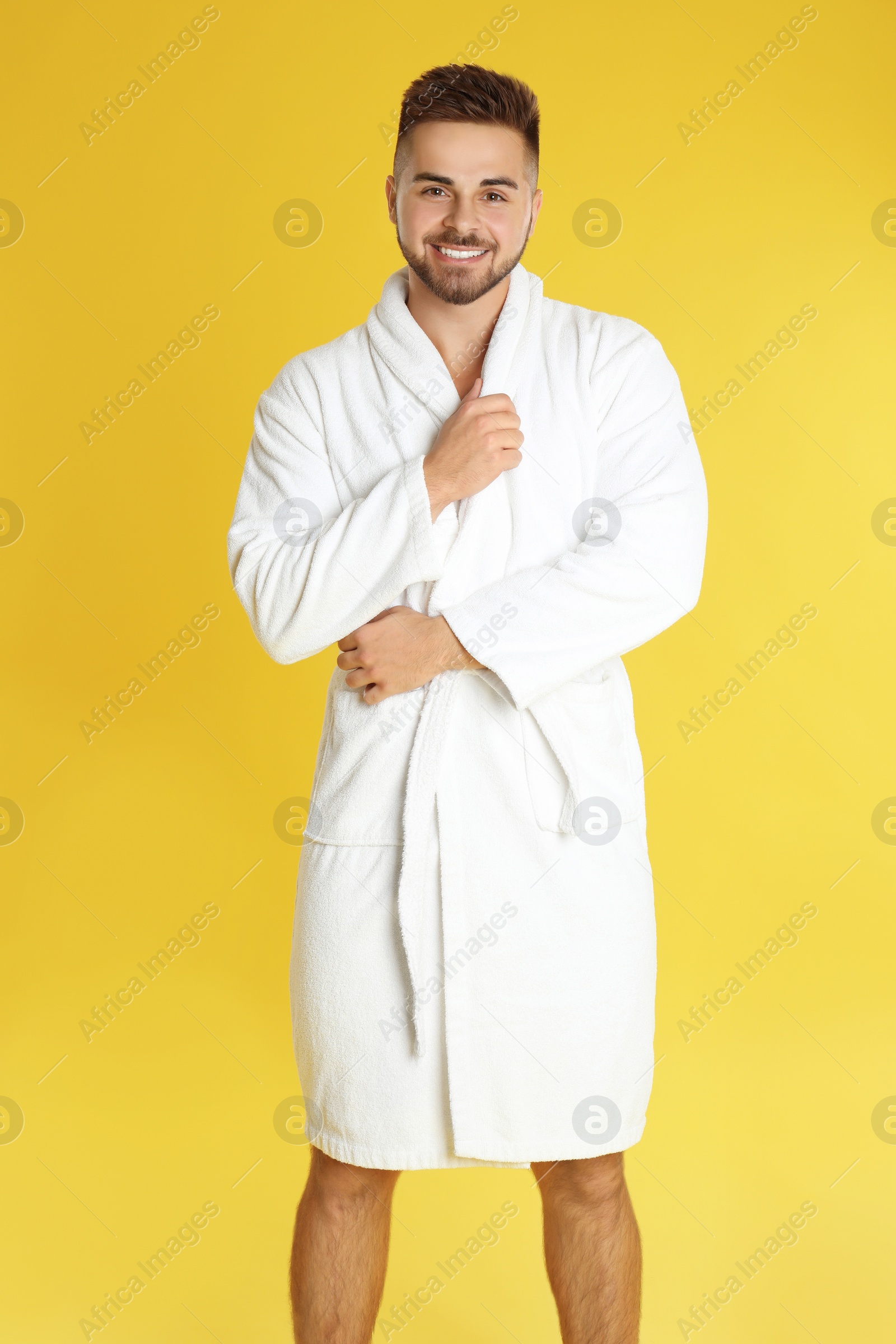 Photo of Happy young man in bathrobe on yellow background