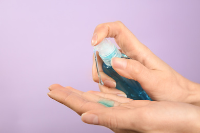 Photo of Woman applying antiseptic gel on lilac background, closeup