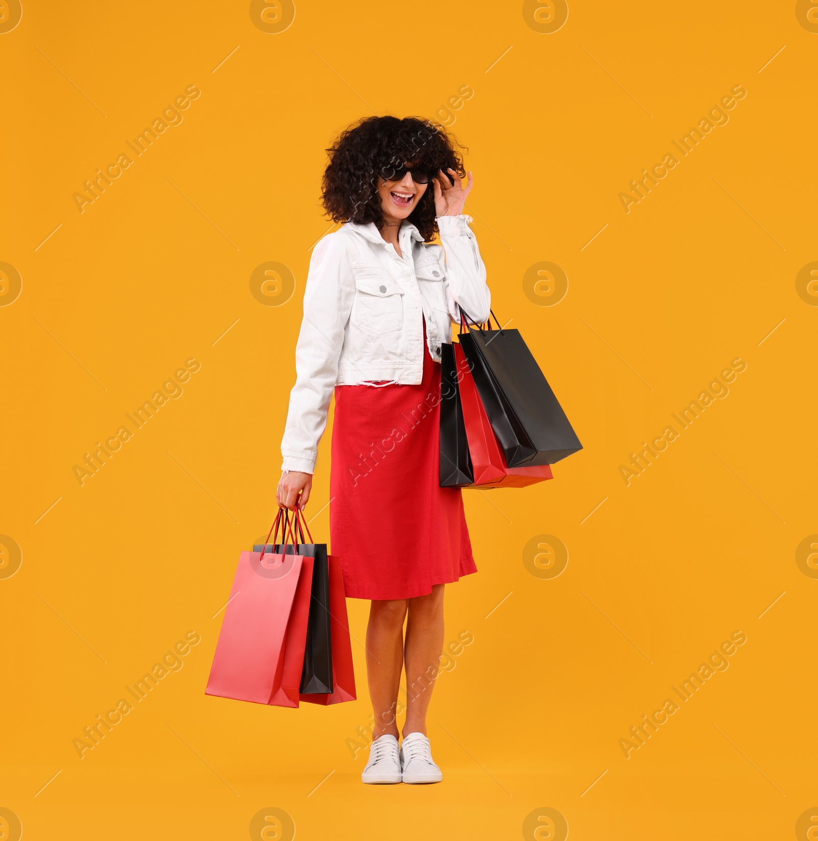 Photo of Happy young woman with shopping bags and stylish sunglasses on yellow background. Space for text