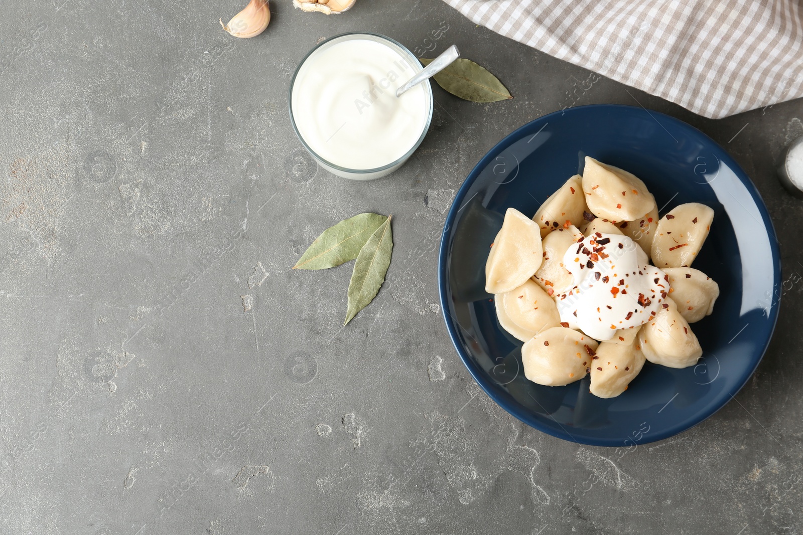 Photo of Delicious cooked dumplings with sour cream on grey table, flat lay. Space for text