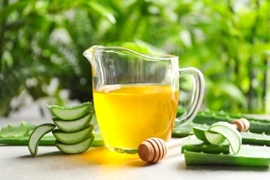 Fresh aloe vera leaves and jug of honey on table against blurred background