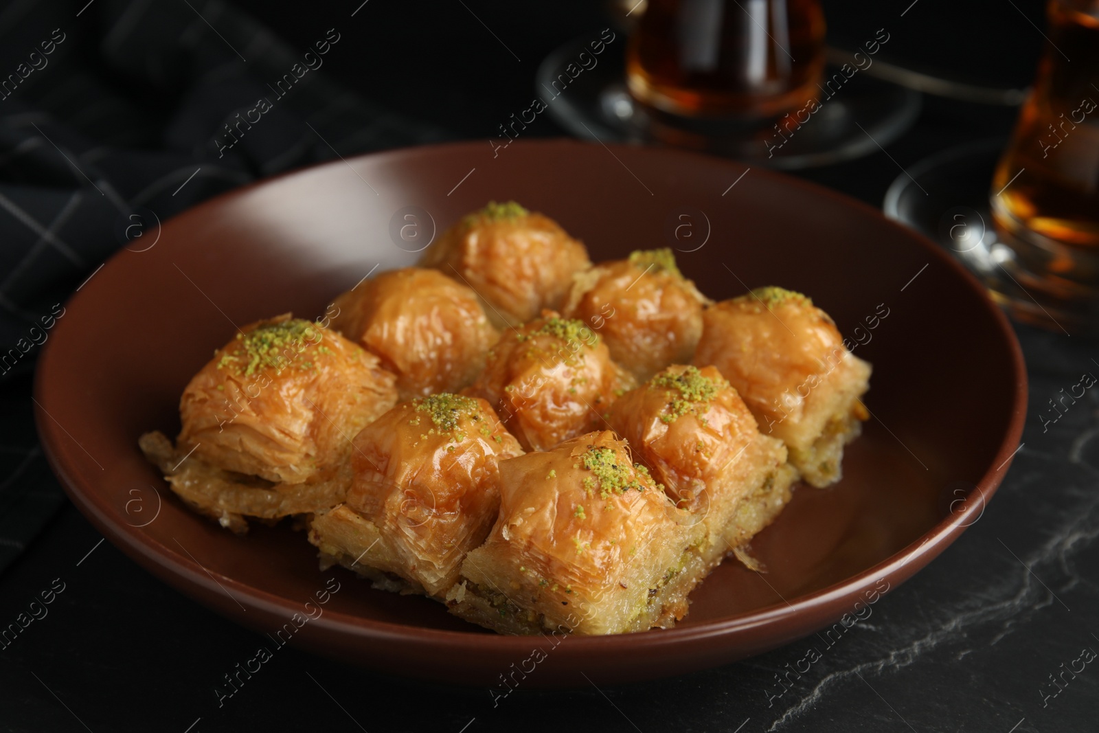 Photo of Delicious sweet baklava in bowl on black table, closeup