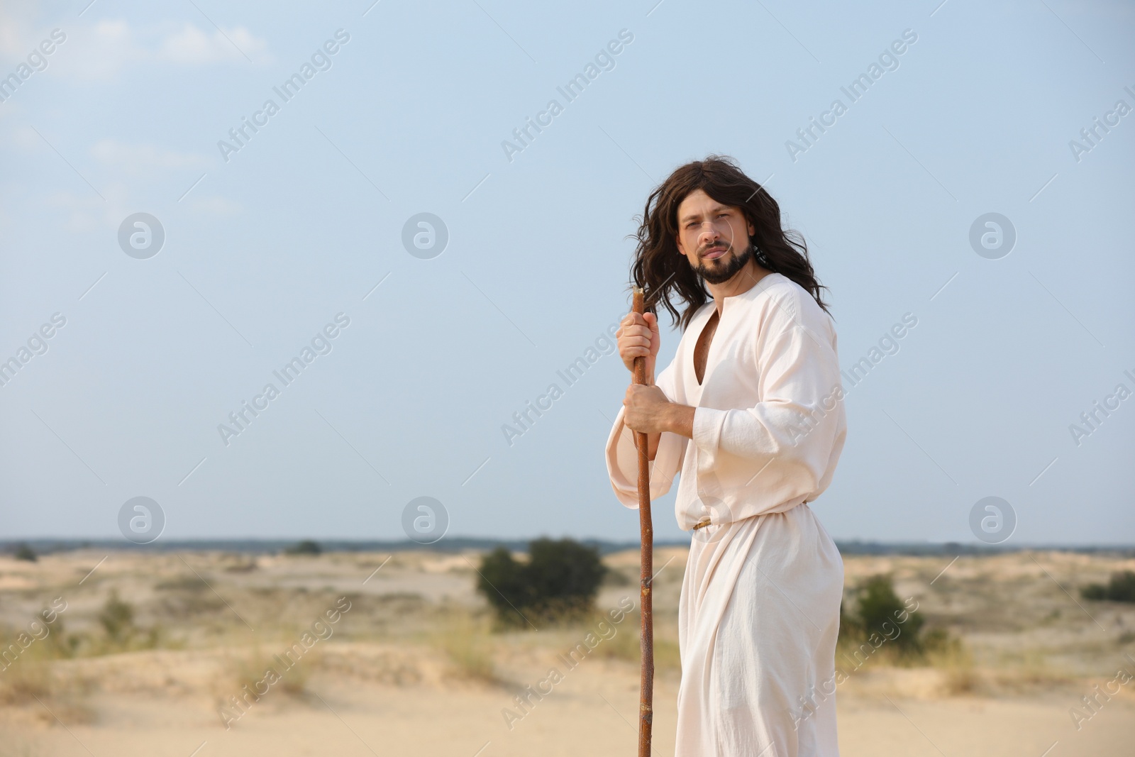 Photo of Jesus Christ walking with stick in desert. Space for text