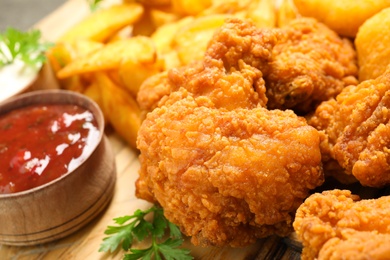 Tasty deep fried chicken pieces with sauce on serving board, closeup