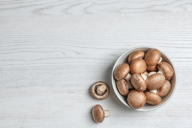 Photo of Bowl of fresh champignon mushrooms on wooden background, top view with space for text