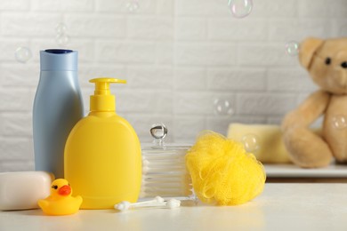 Baby cosmetic products, bath duck, sponge and cotton swabs on white table against soap bubbles