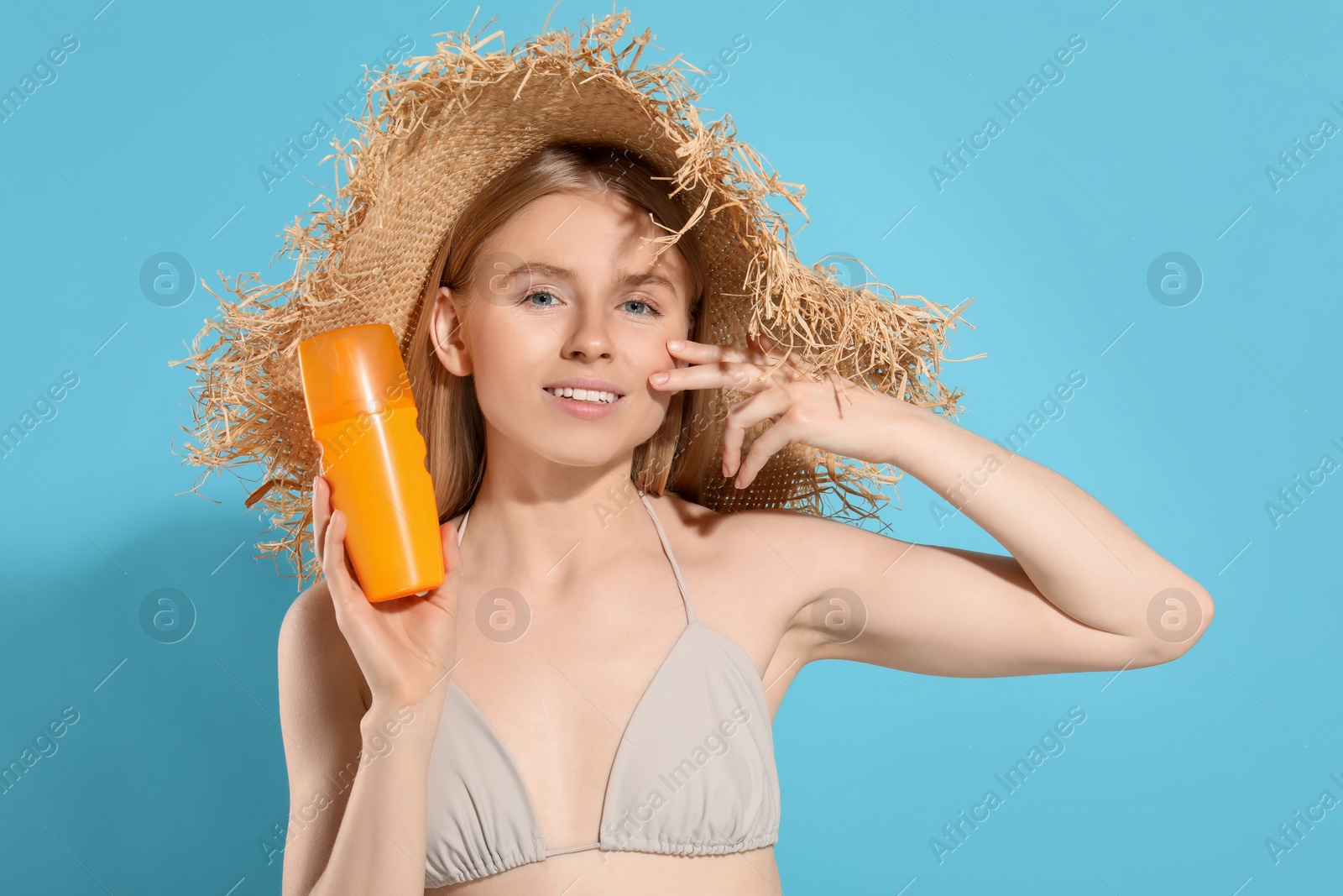 Photo of Beautiful young woman in straw hat with sun protection cream on light blue background