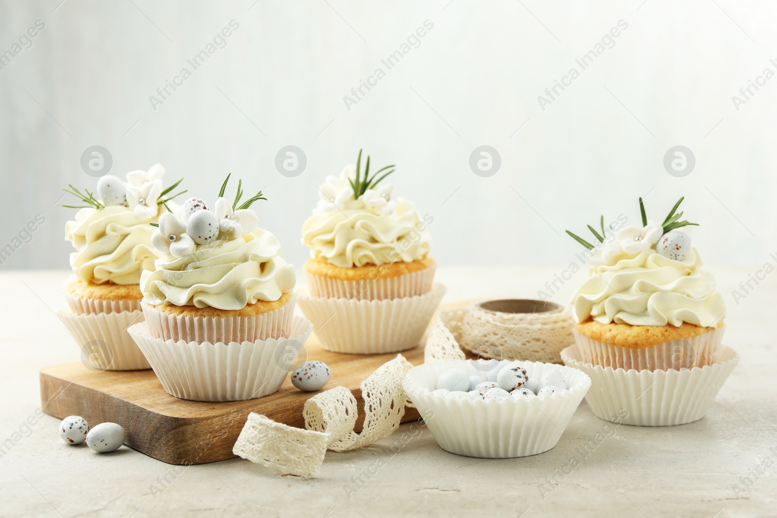 Photo of Tasty Easter cupcakes with vanilla cream, candies and ribbon on gray table