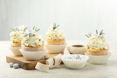 Photo of Tasty Easter cupcakes with vanilla cream, candies and ribbon on gray table