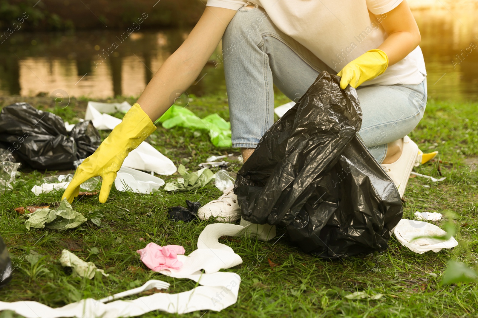 Photo of Woman with plastic bag collecting garbage in park, closeup