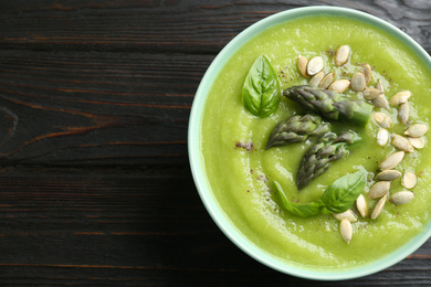 Photo of Delicious asparagus soup in bowl on black wooden table, top view. Space for text