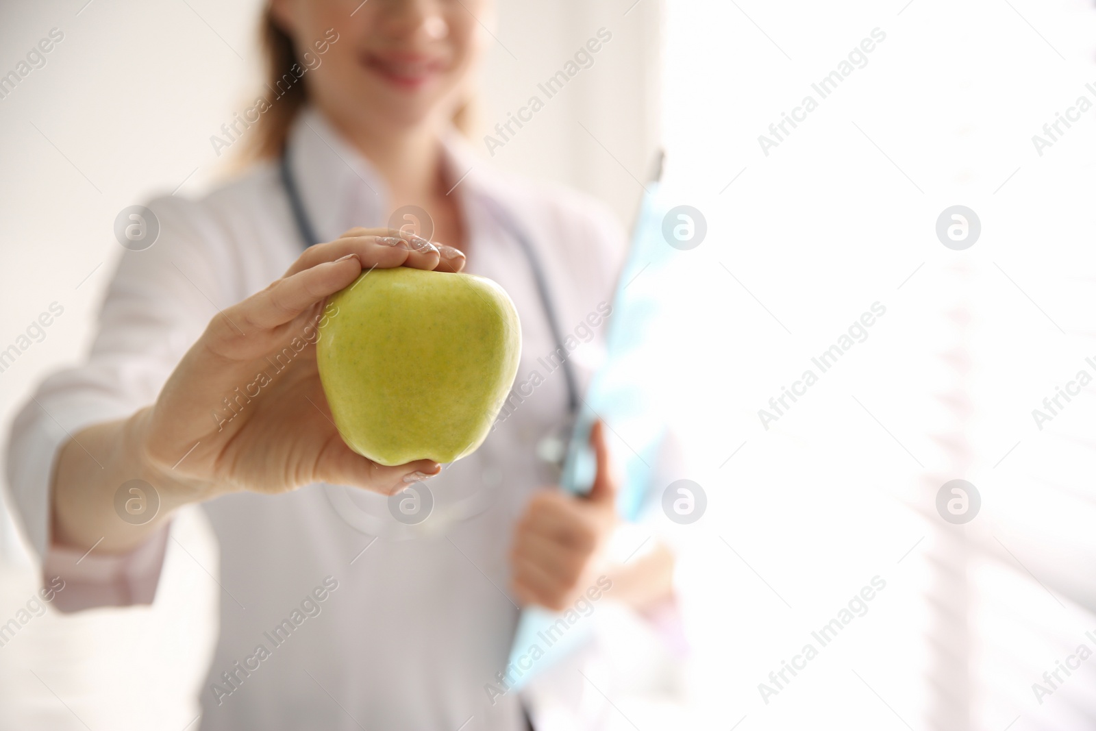 Photo of Nutritionist with apple near window in office, closeup. Space for text