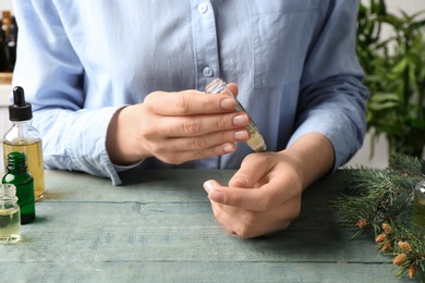 Photo of Woman applying essential oil on wrist at wooden table, closeup