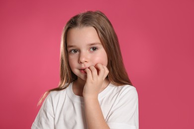 Photo of Cute little girl biting her nails on pink background