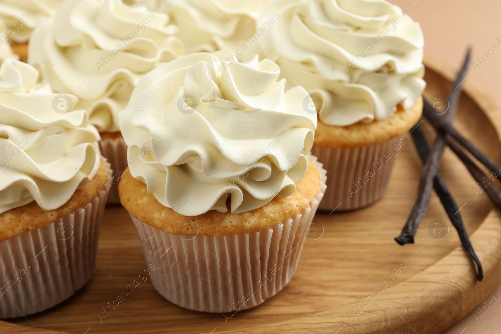 Photo of Tasty cupcakes with cream and vanilla pods on beige table, closeup