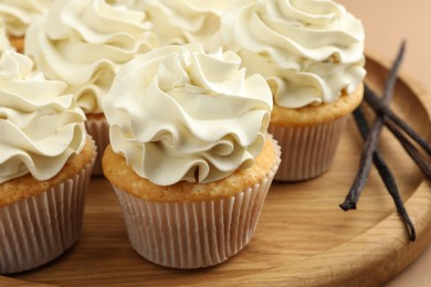 Photo of Tasty cupcakes with cream and vanilla pods on beige table, closeup