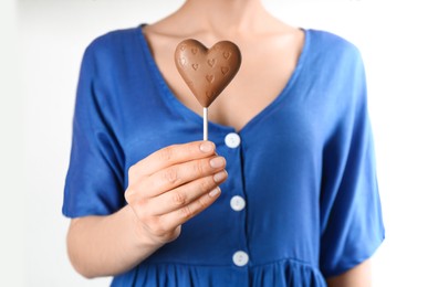 Photo of Woman holding heart shaped lollipop made of chocolate on white background, closeup