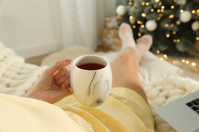 Photo of Woman with cup of tea sitting on sofa, closeup. Christmas celebration